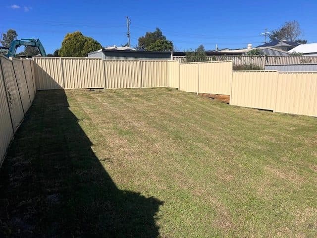 Back yard mown short beside a cream fence after a clean-up