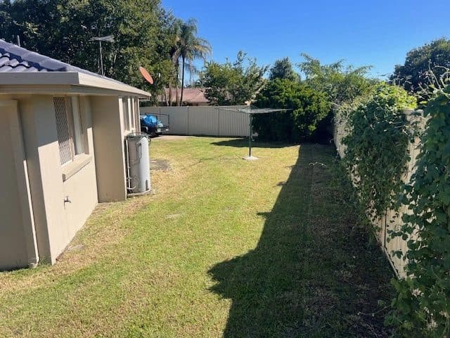 Side of a house with its roofline and gutter above a freshly mown strip of lawn